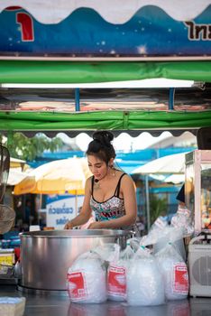 Samut Sakorn, Thailand - February 15, 2020 : Unidentified Asian sexy woman chef cooking a noodle soup with meat ball (kauy-tiew) for sale at Thai street food market or restaurant in Thailand