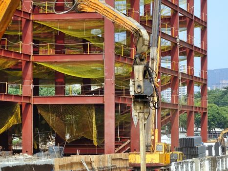 A hydraulic pile driver sinks a large support post into the river bed for bridge construction.