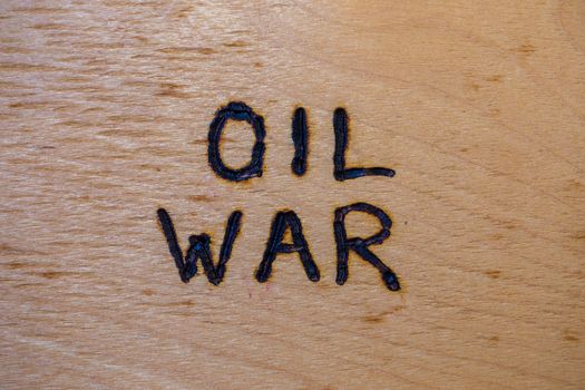the words oil war handwritten on flat bare plywood surface with woodburner.