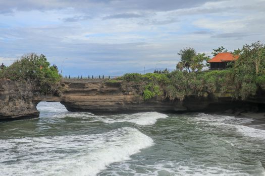 Waves arrive at a rock cliff below Batu Bolong Temple. Tanah Lot temple. Huge hole in rock cliff below Pura Batu Bolong temple. Hindu Temple on the Beatiful Rock in the morning light, Bali, Indonesia.