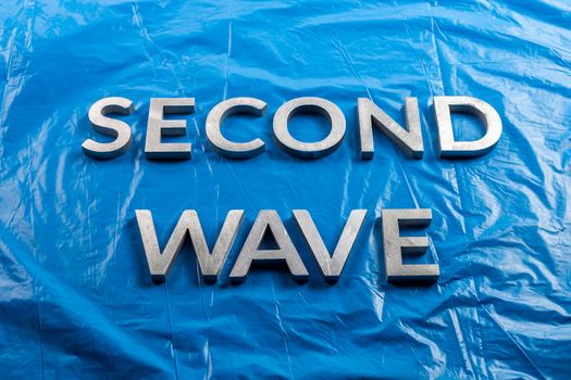 the words second wave laid with silver metal letters over crumpled blue plastic film background in linear perspective.