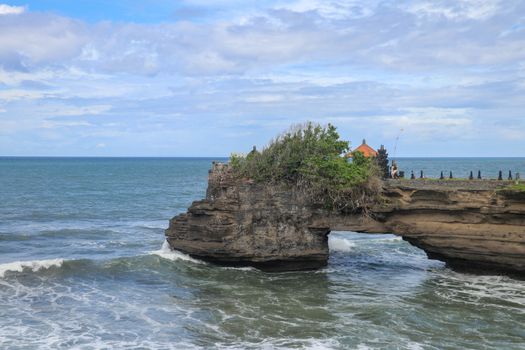 Waves arrive at a rock cliff below Batu Bolong Temple. Tanah Lot temple. Huge hole in rock cliff below Pura Batu Bolong temple. Hindu Temple on the Beatiful Rock in the morning light, Bali, Indonesia.