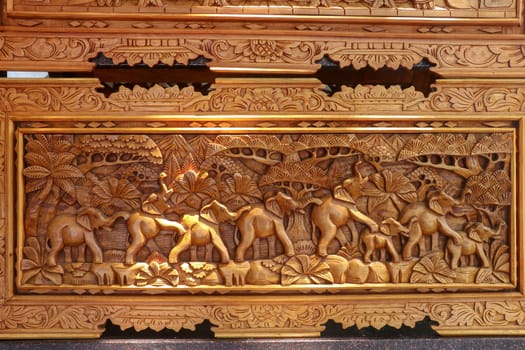 A scene of the last row of elephants in motion carved in wood. Pattern of natural scene. Elephants running through tropical landscape with palm trees in the background. Wood carving decoration. Bali.