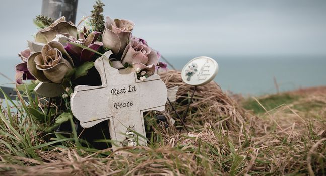 rest in peace written in English on a cross at the edge of a cliff