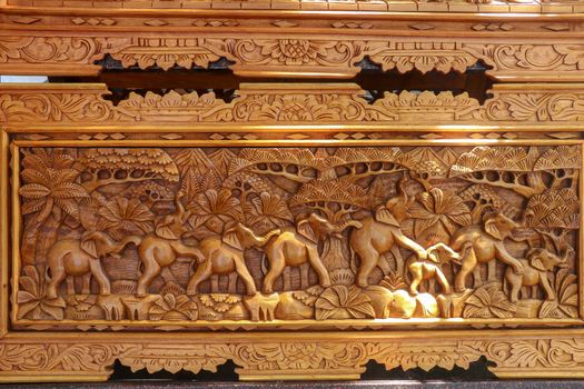A scene of the last row of elephants in motion carved in wood. Pattern of natural scene. Elephants running through tropical landscape with palm trees in the background. Wood carving decoration. Bali.