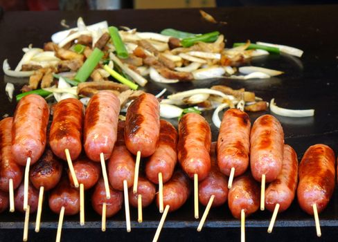 An outdoor vendor roasts fresh sausages and fries pork and leaks