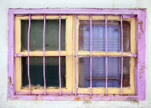 An old window with iron bars and painted in bright pink and yellow colors
