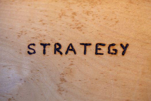 the word strategy handwritten on flat bare plywood surface with woodburner.