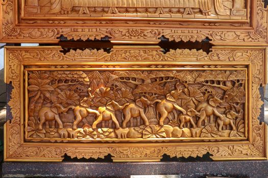 A scene of the last row of elephants in motion carved in wood. Pattern of natural scene. Elephants running through tropical landscape with palm trees in the background. Wood carving decoration. Bali.