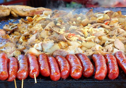 An outdoor vedor cooks meat, vegetables and sausages  on a Teppanyaki griddle