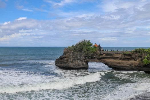 Waves arrive at a rock cliff below Batu Bolong Temple. Tanah Lot temple. Huge hole in rock cliff below Pura Batu Bolong temple. Hindu Temple on the Beatiful Rock in the morning light, Bali, Indonesia.