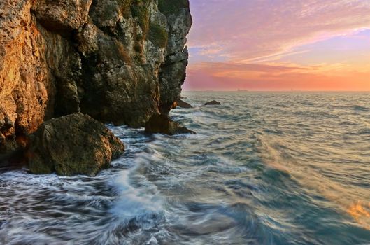 Beautiful rugged cliffs with waves and sunset sky and golden hour