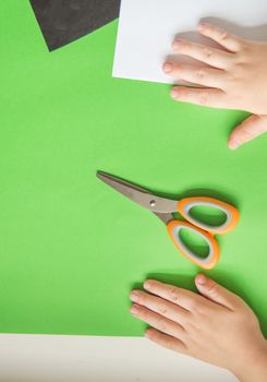 Top view of children's hands on colored paper sheets, colored cardboard and scissors for children's creativity.
