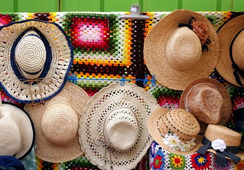 Handmade strawhats with colorful ribbons are displayed by an outdoor vendor