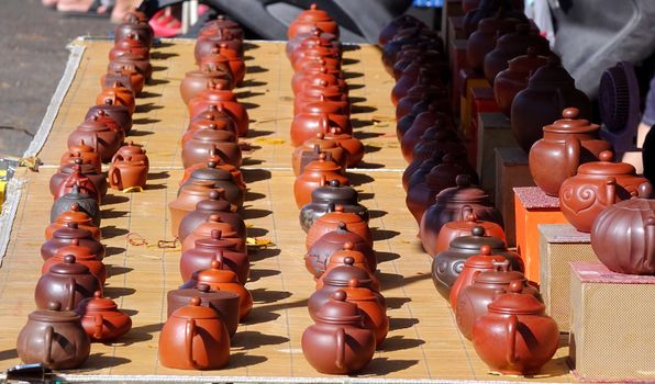 An outdoor vendor sells teapots made from characteristic red clay