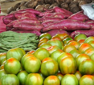 A market stall sells fresh vegetables, such as tomatoes, borad beans and sweet potatoes