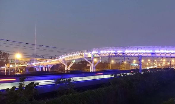 A bike and pedestrian overpass with a speeding train underneath at night
