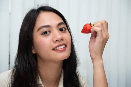 Asian pretty woman holding and eating fresh strawberry is red berry fruit color and sweet juicy with enjoy and happy emotion in concept food, healthy eating in life