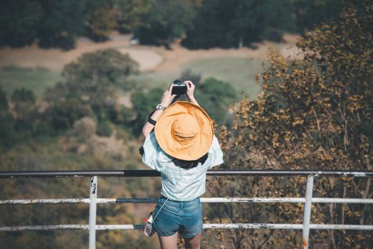 Asian pretty cute woman with hat relax and use smartphone at seaside city landscape viewpoint on mountain with happy and freedom emotion in concept travel, vacation, leisure in life