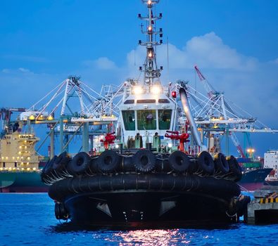 A single tugboat with massive tires fastened to the hull at evening time