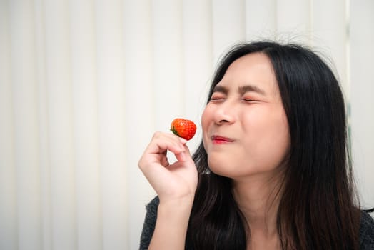 Asian pretty woman holding and eating fresh strawberry is red berry fruit color and sweet juicy with enjoy and happy emotion in concept food, healthy eating in life