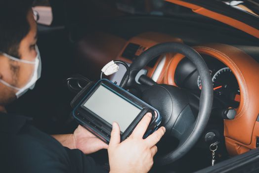 Car mechanic or serviceman checking a car engine by OBD-II electric tools for fix and repair problem at car garage or repair shop