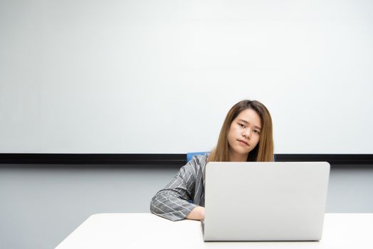 Asian woman is student, businesswoman working by computer notebook, laptop in office meeting room with whiteboard in background with happy and relax emotion in concept working woman, success in life