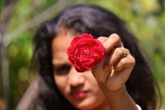 The blurred face of a young girl giving a red rose flower in open hairs