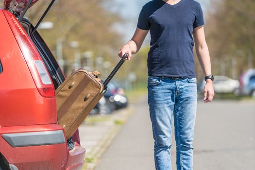 The young man pulls luggage from the car trunk.