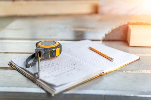 meter, exercise book and pencil on workbench with circular saw in carpentry.