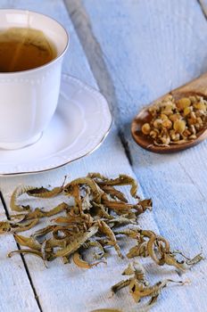 Cup of chamomile and herbs on wooden table in the kitchen.