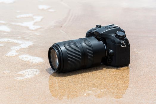 DSLR camera with telephoto lens on a beach it wet from water sea wave when travel and test using in the extreme environment demo waterproof by photographer