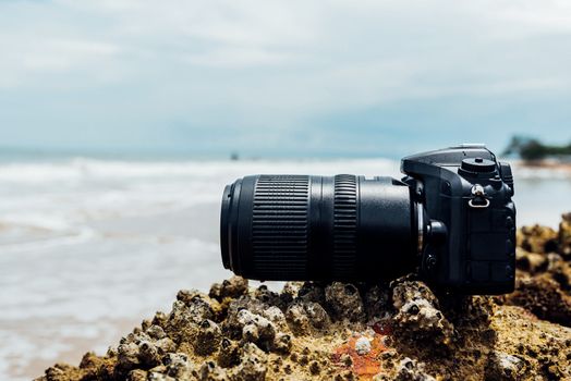 DSLR camera with telephoto lens wet from water sea wave at stone beach when travel and test using in the extreme environment demo waterproof by photographer