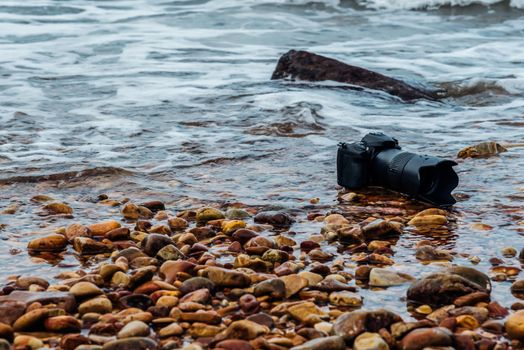 DSLR camera with telephoto lens wet from water sea wave at stone beach when travel and test using in the extreme environment demo waterproof by photographer