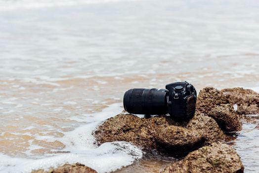 DSLR camera with telephoto lens wet from water sea wave at stone beach when travel and test using in the extreme environment demo waterproof by photographer