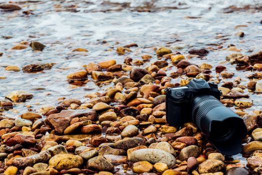 DSLR camera with telephoto lens wet from water sea wave at stone beach when travel and test using in the extreme environment demo waterproof by photographer