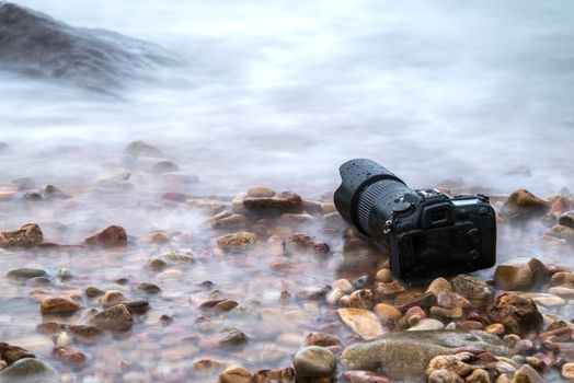 DSLR camera with telephoto lens wet from water sea wave at stone beach when travel and test using in the extreme environment demo waterproof by photographer