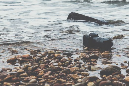 DSLR camera with telephoto lens wet from water sea wave at stone beach when travel and test using in the extreme environment demo waterproof by photographer