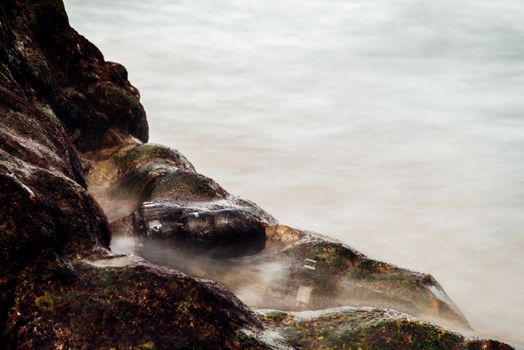 DSLR camera with telephoto lens wet from water sea wave at stone beach when travel and test using in the extreme environment demo waterproof by photographer