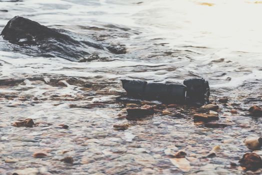 DSLR camera with telephoto lens wet from water sea wave at stone beach when travel and test using in the extreme environment demo waterproof by photographer