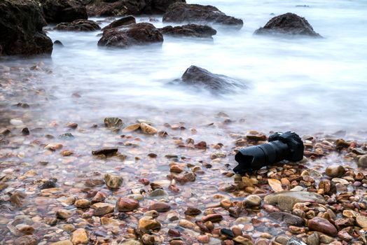 DSLR camera with telephoto lens wet from water sea wave at stone beach when travel and test using in the extreme environment demo waterproof by photographer