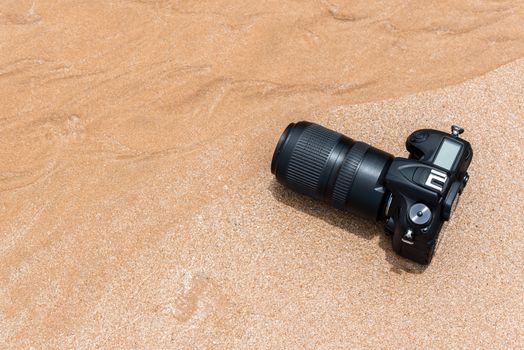 DSLR camera with telephoto lens on a beach it wet from water sea wave when travel and test using in the extreme environment demo waterproof by photographer