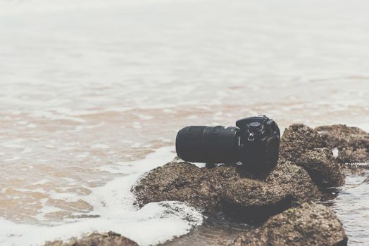 DSLR camera with telephoto lens wet from water sea wave at stone beach when travel and test using in the extreme environment demo waterproof by photographer