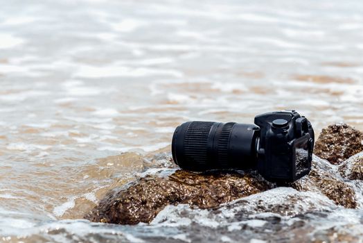 DSLR camera with telephoto lens wet from water sea wave at stone beach when travel and test using in the extreme environment demo waterproof by photographer