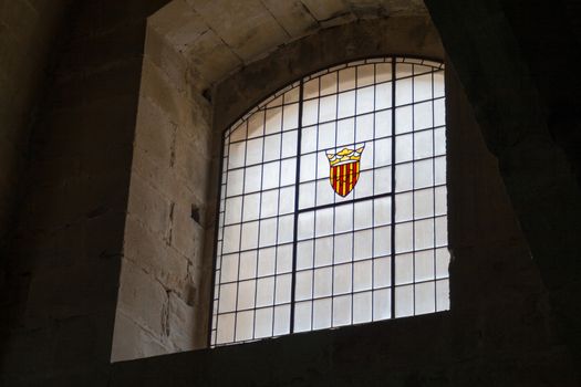 dungeon old window in darkness with the Coat of arms of the Crown of Aragon. Cistercian Monastery of Poblet in the Catalonia region of Spain. Declared a UNESCO World Heritage Site ref. 518rev