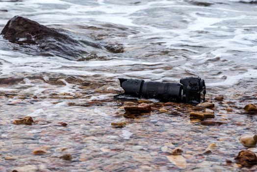 DSLR camera with telephoto lens wet from water sea wave at stone beach when travel and test using in the extreme environment demo waterproof by photographer