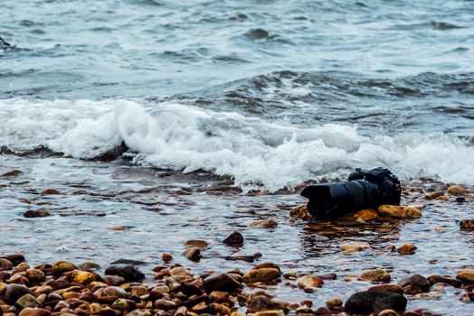 DSLR camera with telephoto lens wet from water sea wave at stone beach when travel and test using in the extreme environment demo waterproof by photographer