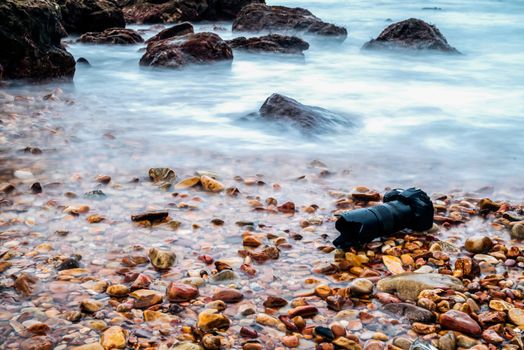 DSLR camera with telephoto lens wet from water sea wave at stone beach when travel and test using in the extreme environment demo waterproof by photographer
