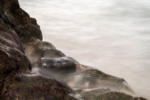 DSLR camera with telephoto lens wet from water sea wave at stone beach when travel and test using in the extreme environment demo waterproof by photographer