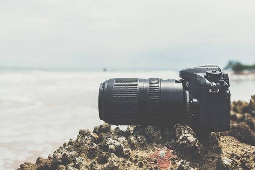 DSLR camera with telephoto lens wet from water sea wave at stone beach when travel and test using in the extreme environment demo waterproof by photographer